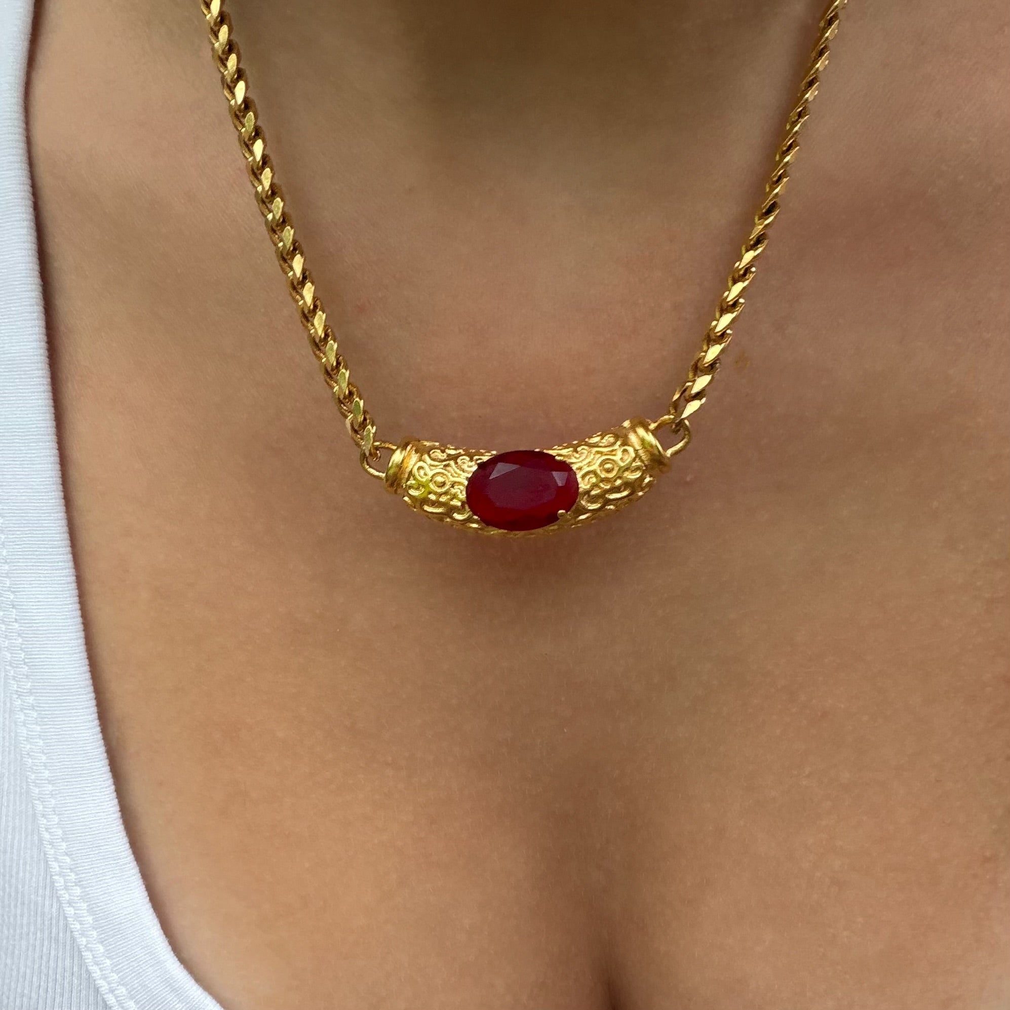 Gold chain necklace with a deep red oval stone on a textured bar