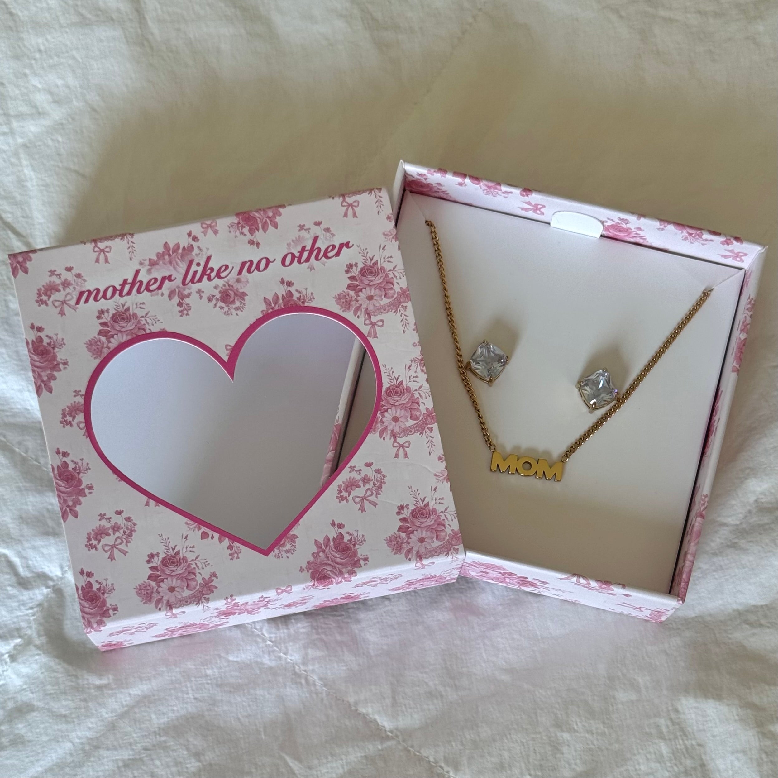 Open pink floral gift box printed mother like no other holding a gold tone MOM necklace and clear square stud earrings