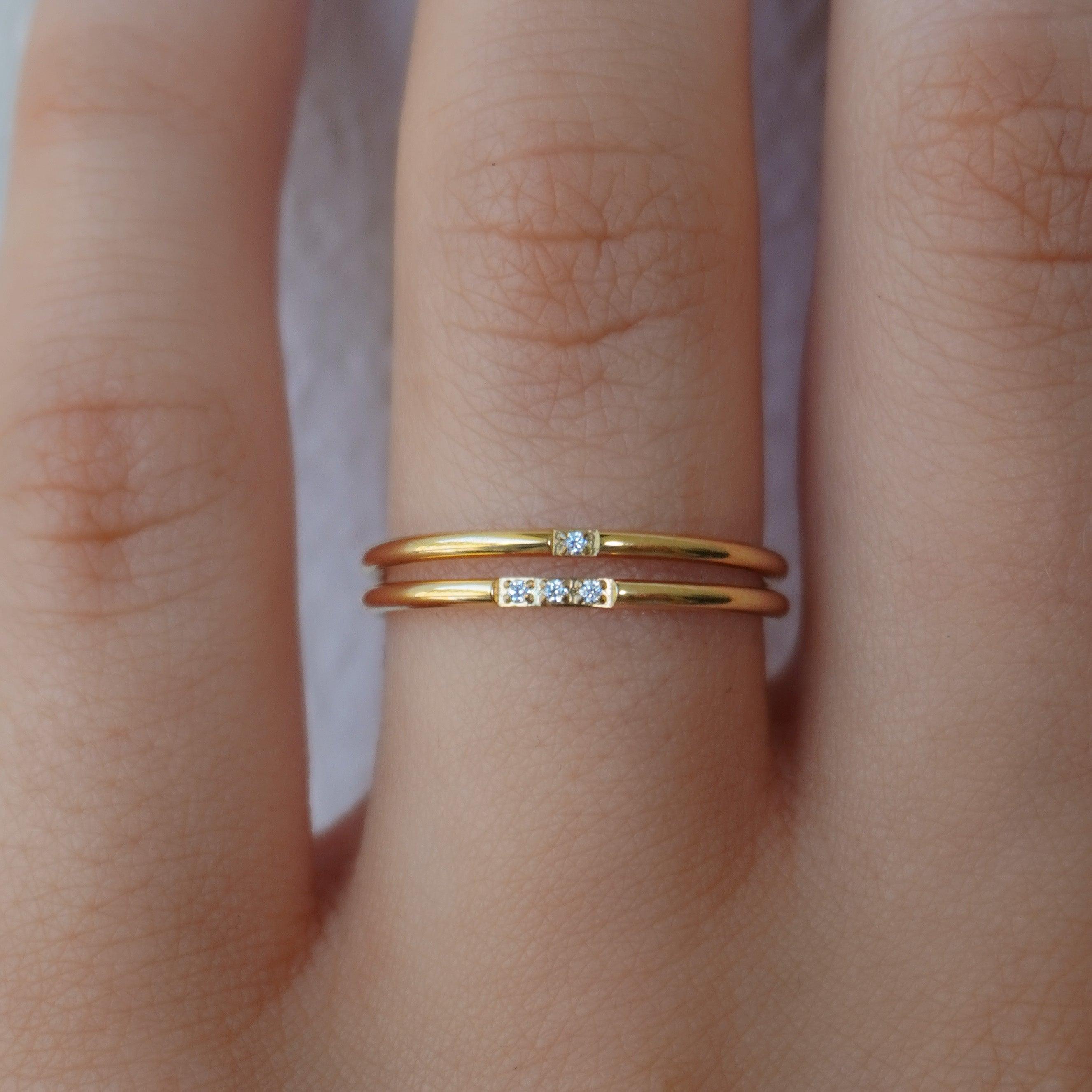 Two thin gold tone stacking rings set with small clear stones worn together on one finger