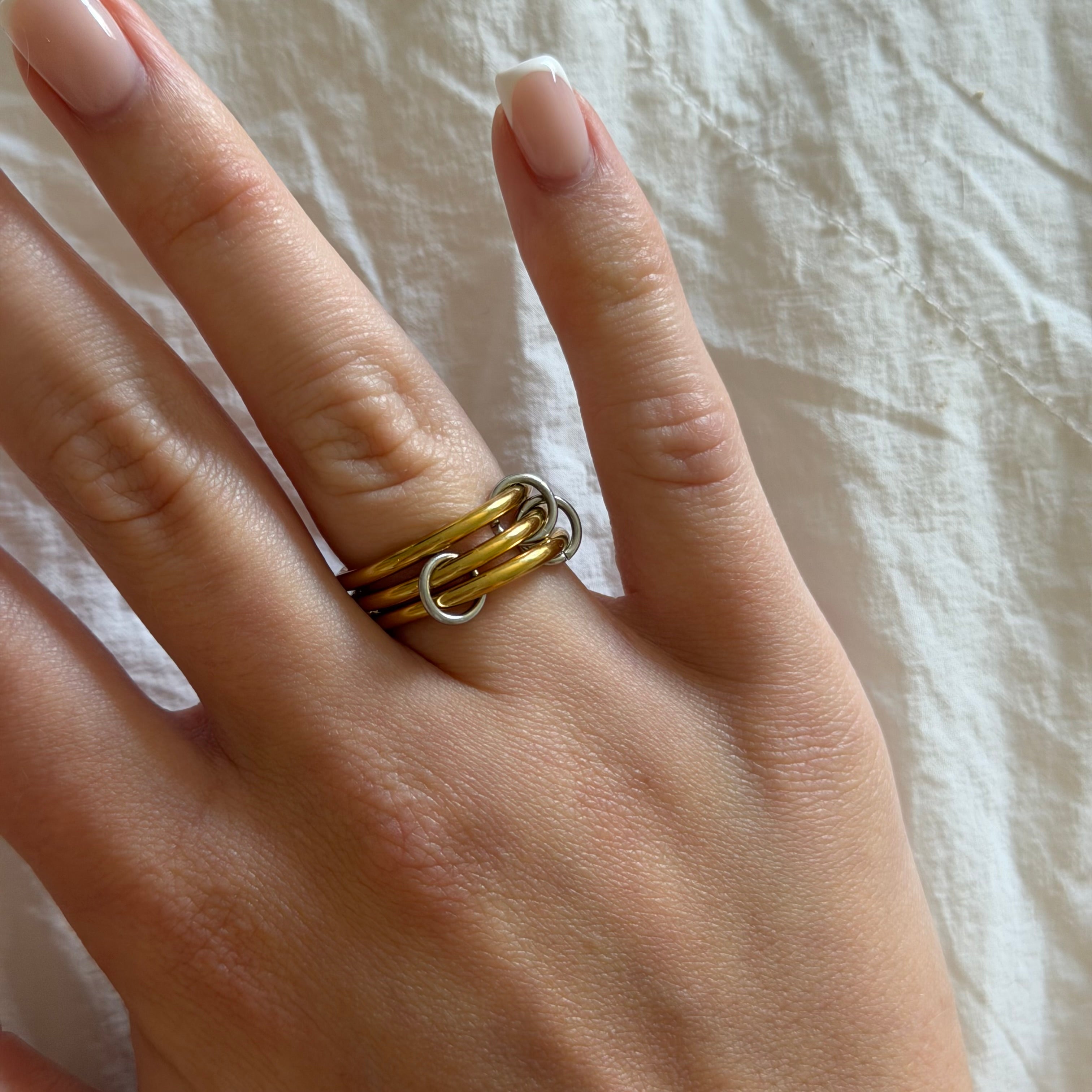 Hand wearing a stack of interlocking gold tone and silver tone ring bands