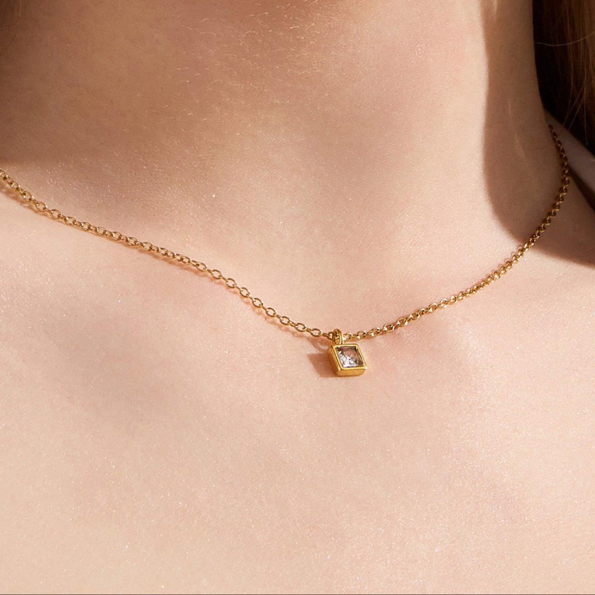 Gold chain necklace with a small square stone pendant worn at the collarbone