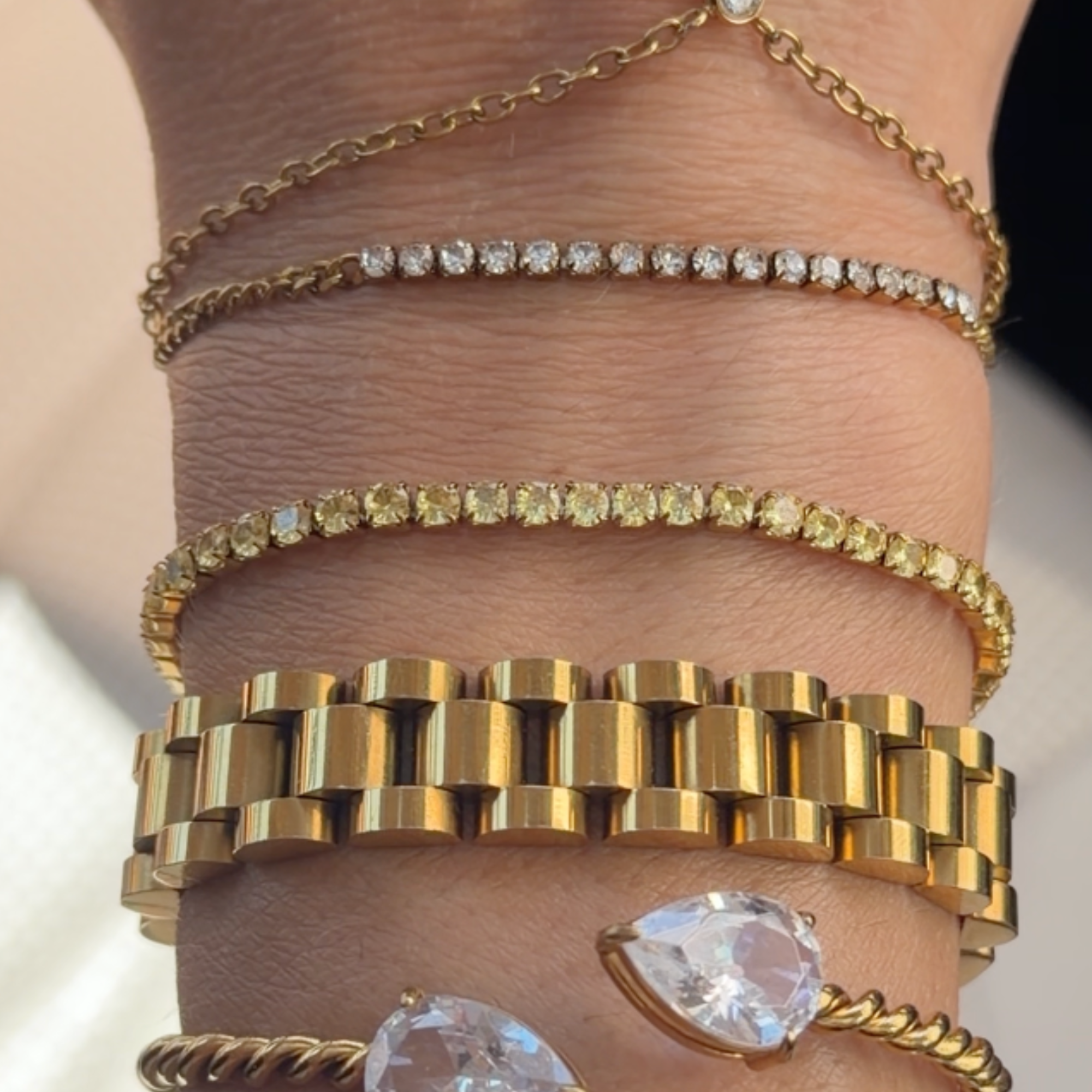 Yellow stone tennis bracelet stacked with gold chain and link bracelets on a wrist